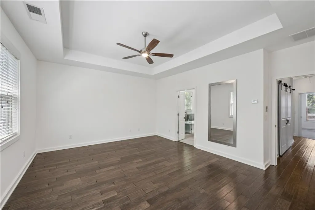 Unfurnished bedroom with a raised ceiling, ceiling fan, and dark wood-style flooring