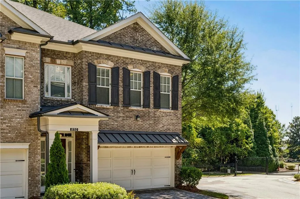 View of front facade featuring a standing seam roof, brick siding, a metal roof, driveway, and an attached garage
