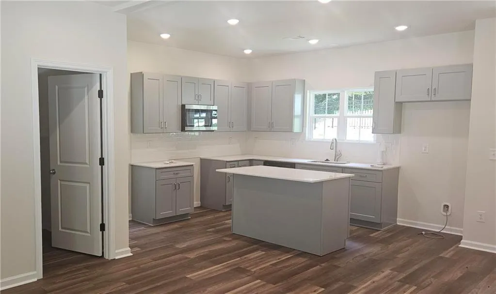 Kitchen with gray cabinets, a center island, dark wood-type flooring, stainless steel microwave, and decorative backsplash