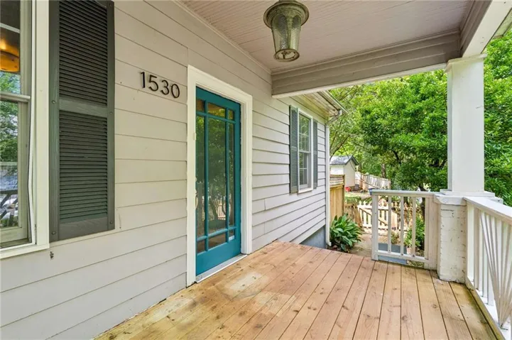 Covered front porch featuring wood plank flooring, a teal glass-paneled entry door, and white painted railings