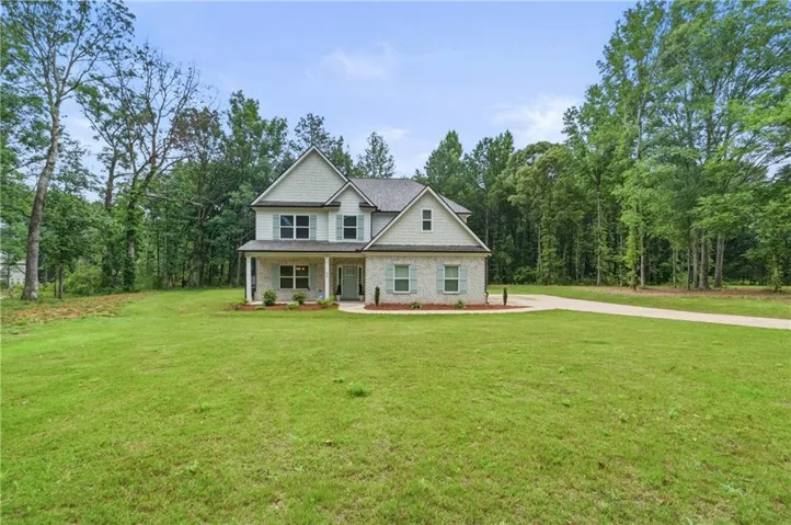 Two-story residence featuring light brick and shingle siding, a covered front porch, and a paved driveway, set on a broad grassy lot with mature trees