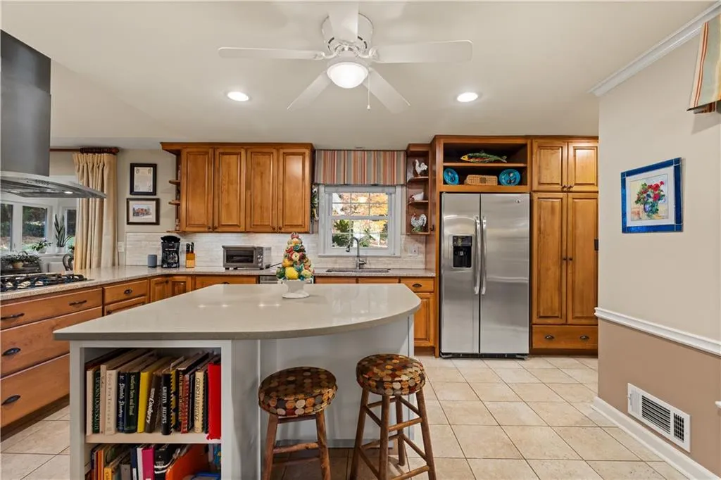 Kitchen featuring open shelves, brown cabinets, a kitchen bar, range hood, and stainless steel appliances