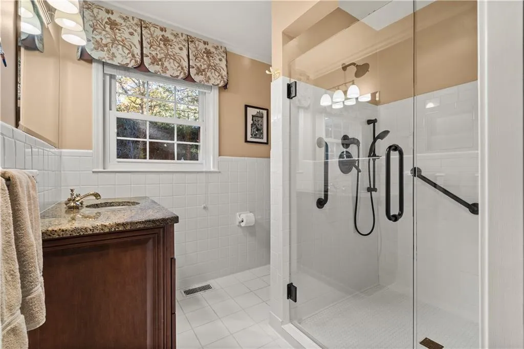 Bathroom with tile walls, vanity, a stall shower, light tile patterned floors, and wainscoting