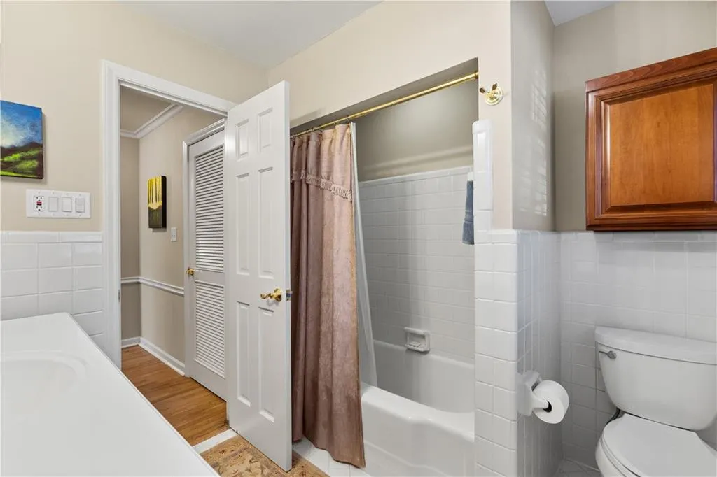 Bathroom featuring tile walls, vanity, shower / bath combo with shower curtain, wainscoting, and light wood-style flooring