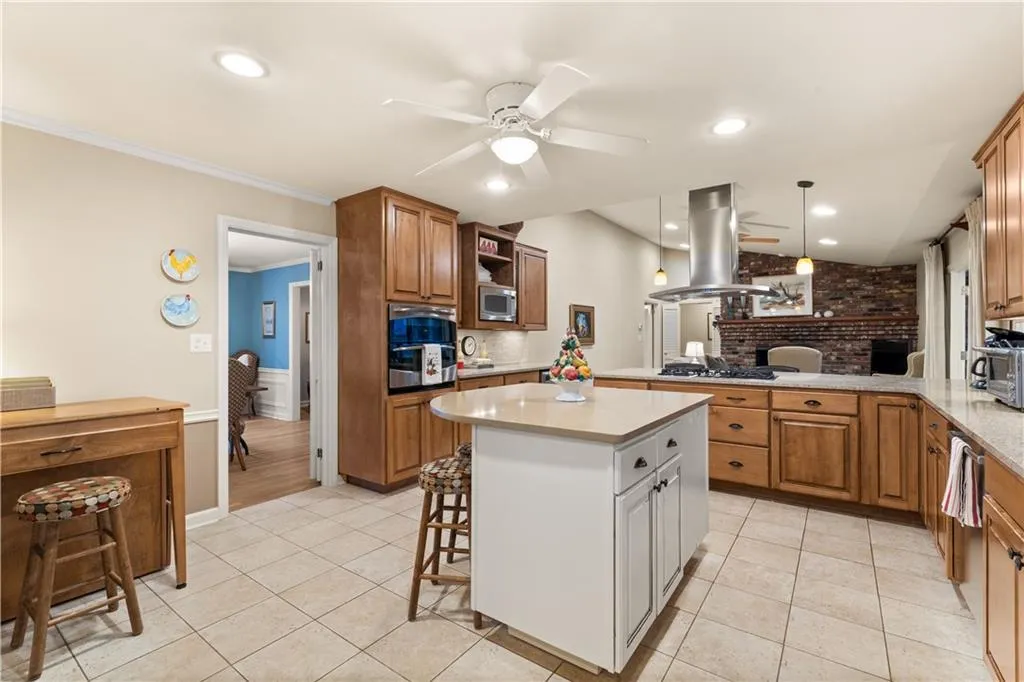 Kitchen with brown cabinetry, a breakfast bar, ceiling fan, recessed lighting, and ornamental molding