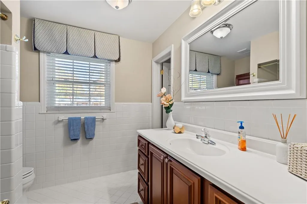 Full bath with tile walls, vanity, a wainscoted wall, and light tile patterned flooring