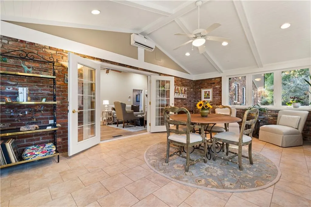 Dining room featuring brick wall, french doors, beamed ceiling, a wall mounted air conditioner, and a ceiling fan
