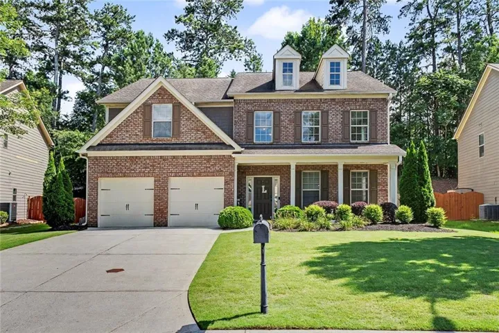 Traditional-style home featuring brick and siding construction, a two-car garage, a covered front porch, and a dormered roofline