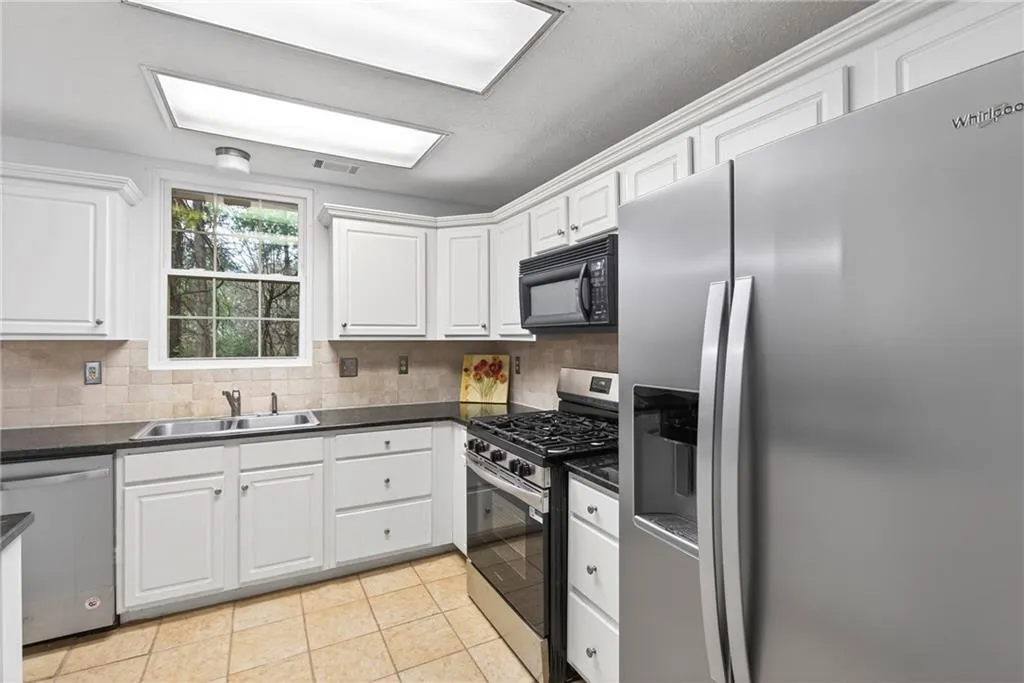 Kitchen with stainless steel appliances, white cabinetry, light tile patterned floors, and tasteful backsplash