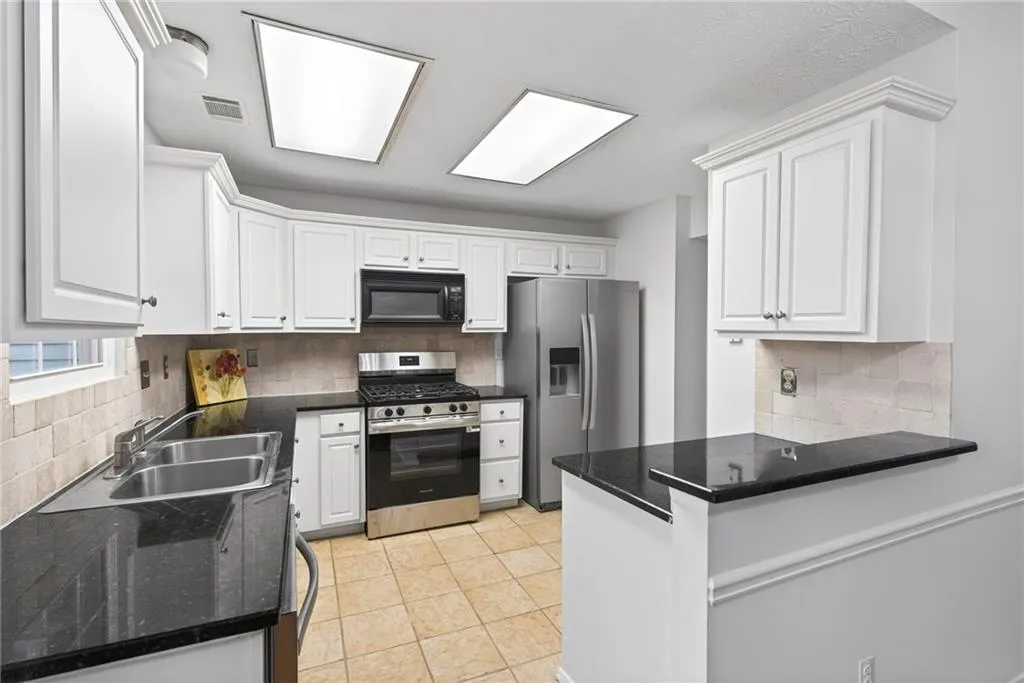 Kitchen featuring stainless steel appliances, white cabinetry, decorative backsplash, a peninsula, and light tile patterned floors