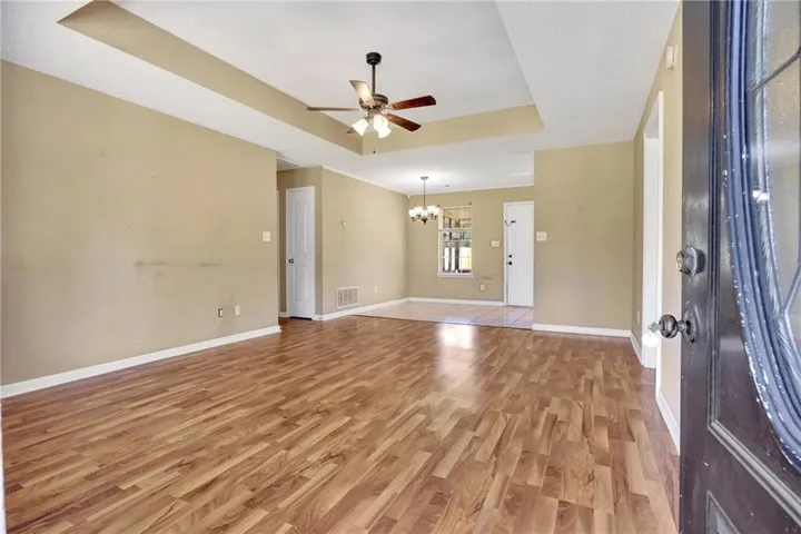 Wood-finish flooring throughout, tray ceiling with a ceiling fan, and recessed dining area with tile flooring and chandelier