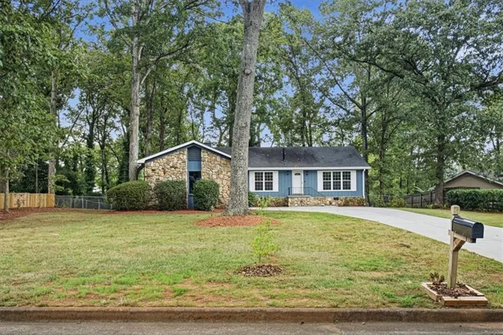 Stone-accented exterior with blue siding, a dark roof, and a front porch, complemented by a concrete driveway and mature trees