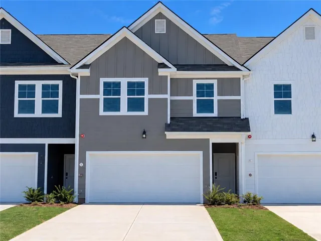 Contemporary townhome exterior featuring a two-car garage, multiple window configurations, board and batten siding, and architectural shingles