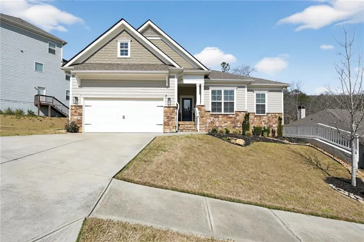 Exterior featuring stone and siding finishes, an attached garage, a concrete driveway, and established landscaping
