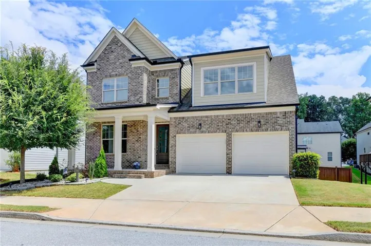 Two-story exterior with brick and siding facade, covered entry with columns, two-car garage, and established landscaping