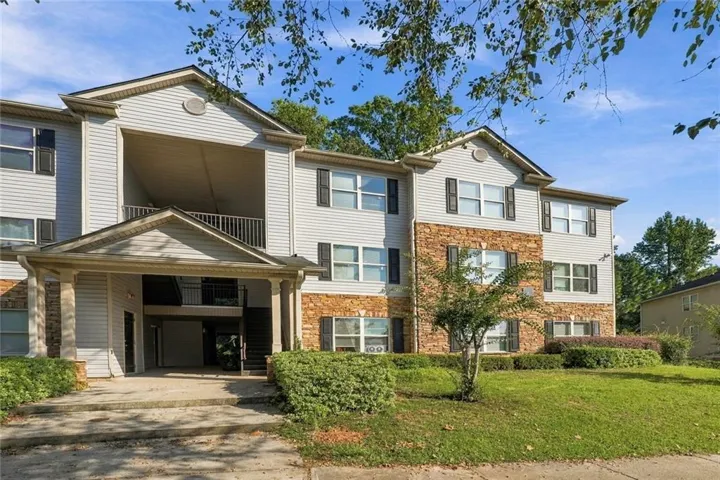 Multi-story building featuring horizontal siding, stone veneer accents, individual balconies, and a covered entry