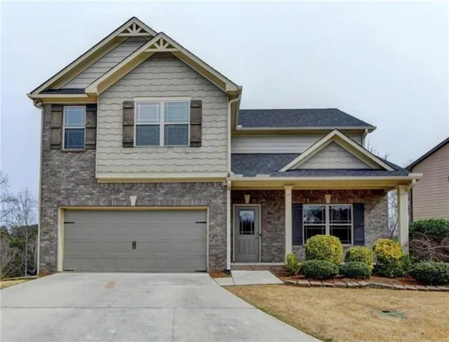 Two-story residence featuring a brick and siding facade, an attached front-entry garage, a covered front porch, and a paved driveway