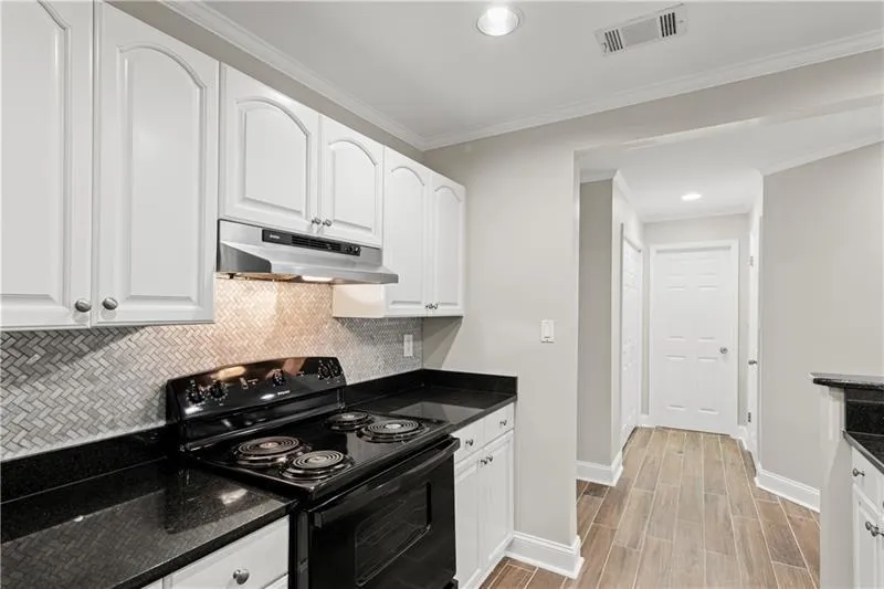 Kitchen with black range with electric stovetop, white cabinets, under cabinet range hood, crown molding, and recessed lighting