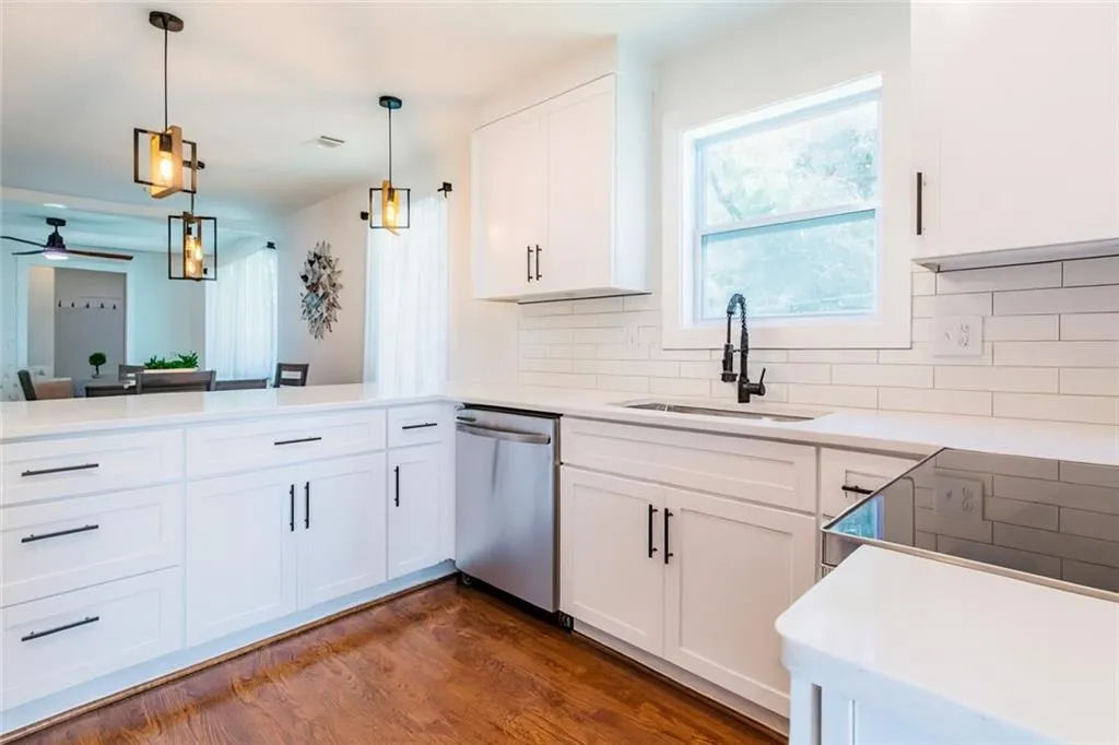 Kitchen featuring backsplash, dark wood-type flooring, dishwasher, hanging light fixtures, and white cabinetry