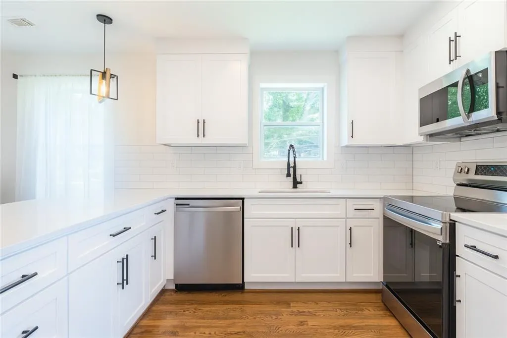 Kitchen featuring appliances with stainless steel finishes, wood finished floors, light countertops, and white cabinets