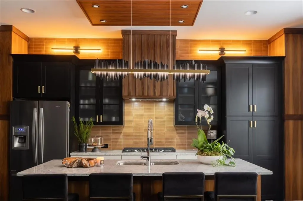 Modern cabinetry with walnut wood accents, brushed gold hardware, drop ceiling, columns, and designer lighting
