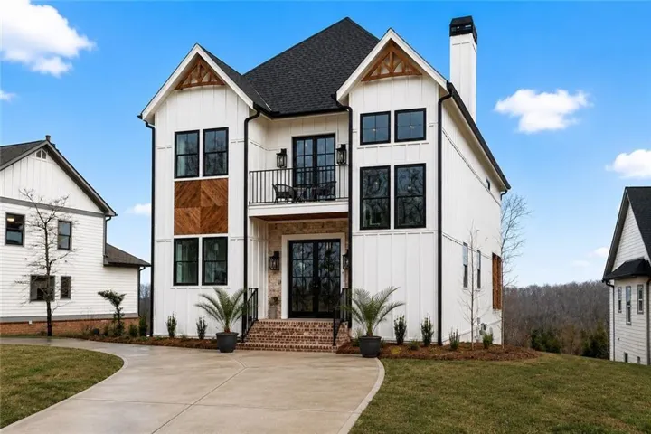 Modern farmhouse exterior featuring white board and batten siding, a black shingle roof, and striking black-framed windows