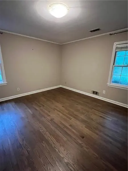 Empty room featuring plenty of natural light, dark wood finished floors, and crown molding