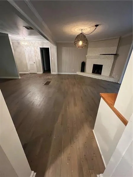 Unfurnished living room featuring dark wood-style floors, ornamental molding, and a large fireplace