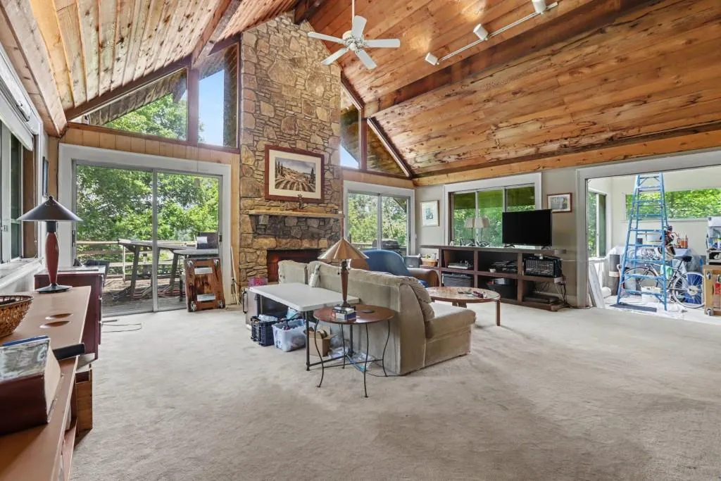 Distinctive architectural character, including soaring Vaulted Wood Ceilings, exposed beams, a dramatic Stone Fireplace, and walls of windows that take advantage of the private, wooded surroundings