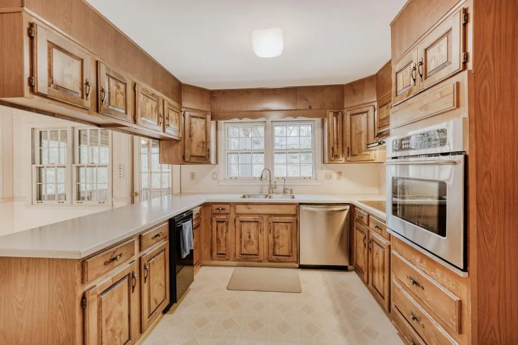 Kitchen featuring light countertops, light floors, stainless steel appliances, a peninsula, and wood finish cabinets