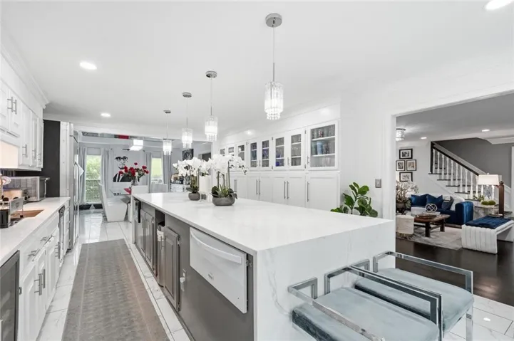 Expansive kitchen featuring a large central island with waterfall edge, integrated appliances, and multiple pendant lights