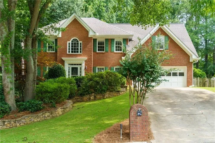 Brick exterior home featuring a two-car garage, manicured landscaping, stone retaining walls, and a prominent arched window above the entry
