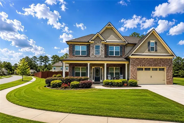 Two-story residence featuring a brick and siding exterior, an attached two-car garage, covered porch, well-maintained lawn, and established landscaping