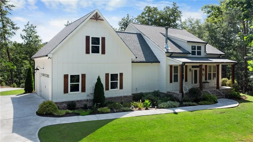 White board and batten exterior featuring dark wood shutters, a covered porch with timber columns, a gabled roofline, and an attached two-car garage