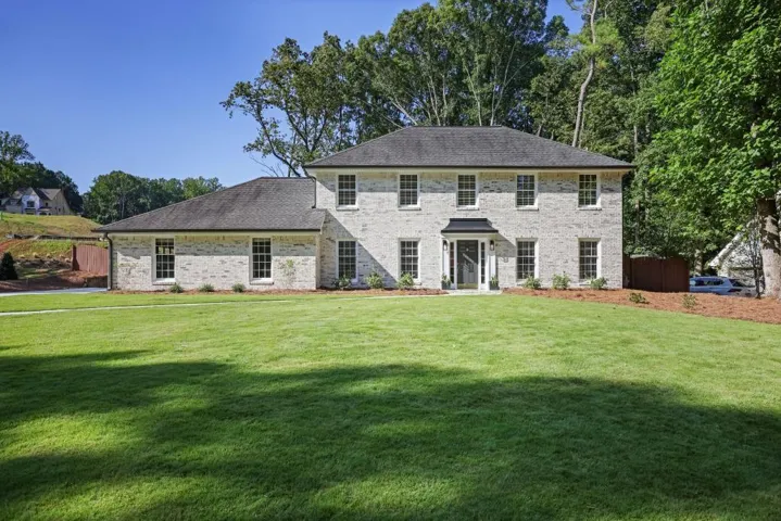 Traditional-style residence featuring a light-colored brick facade, dark shingle roof, and a prominent front entrance with a covered portico