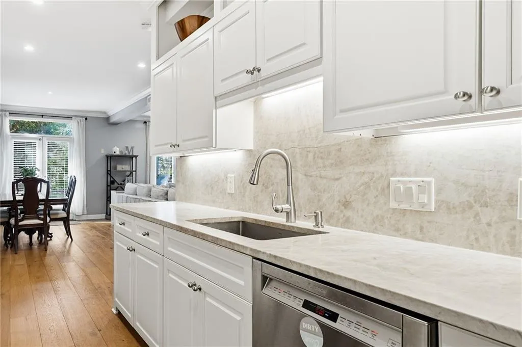 Kitchen featuring white cabinets, light stone counters, ornamental molding, stainless steel dishwasher, and light wood-style floors