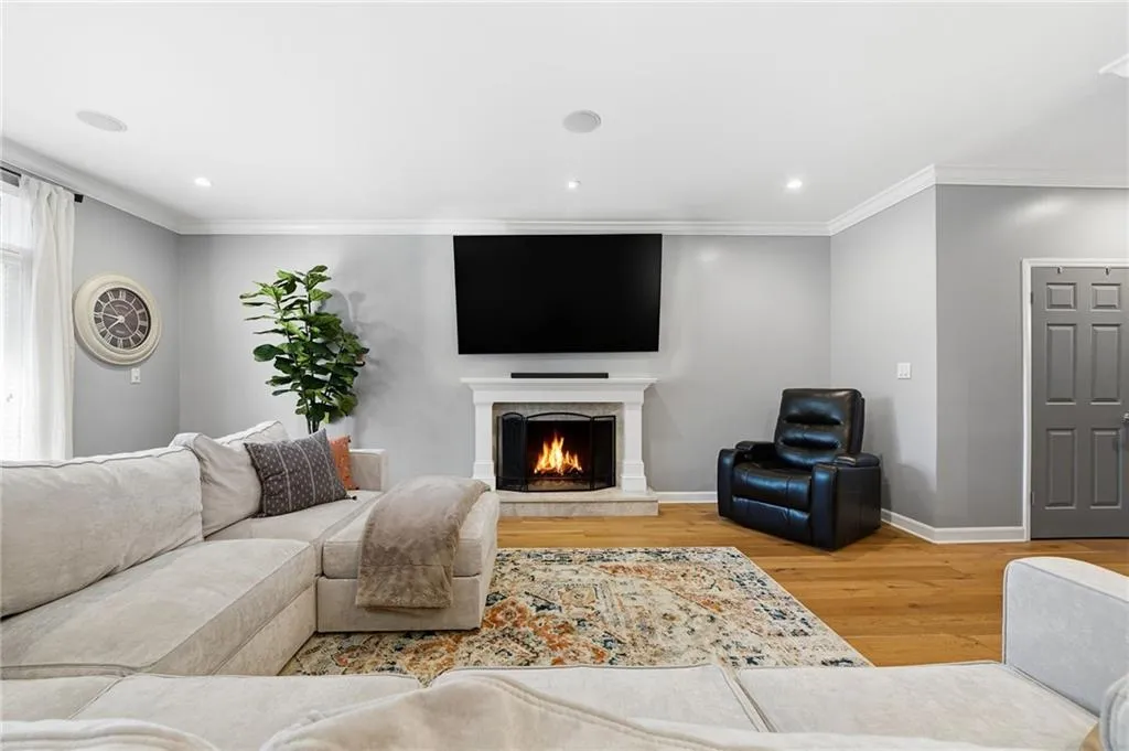 Living room with light wood-style flooring, a warm lit fireplace, crown molding, and recessed lighting