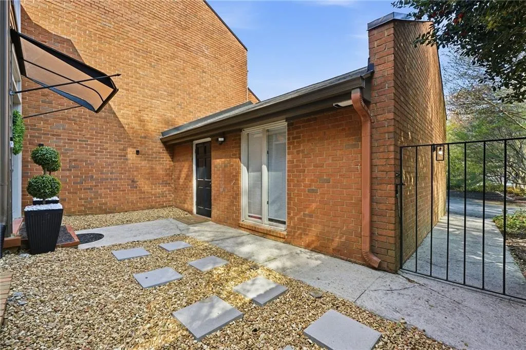 View of side of property with a patio, brick siding, a gate, and a chimney