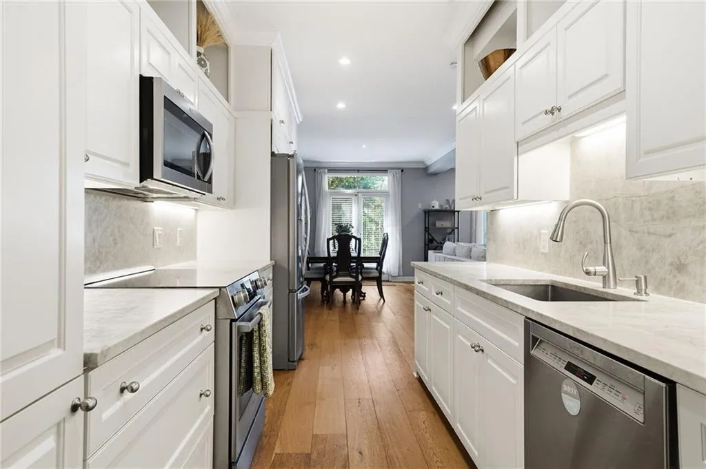 Kitchen with stainless steel appliances, ornamental molding, white cabinets, light wood-style flooring, and light stone counters