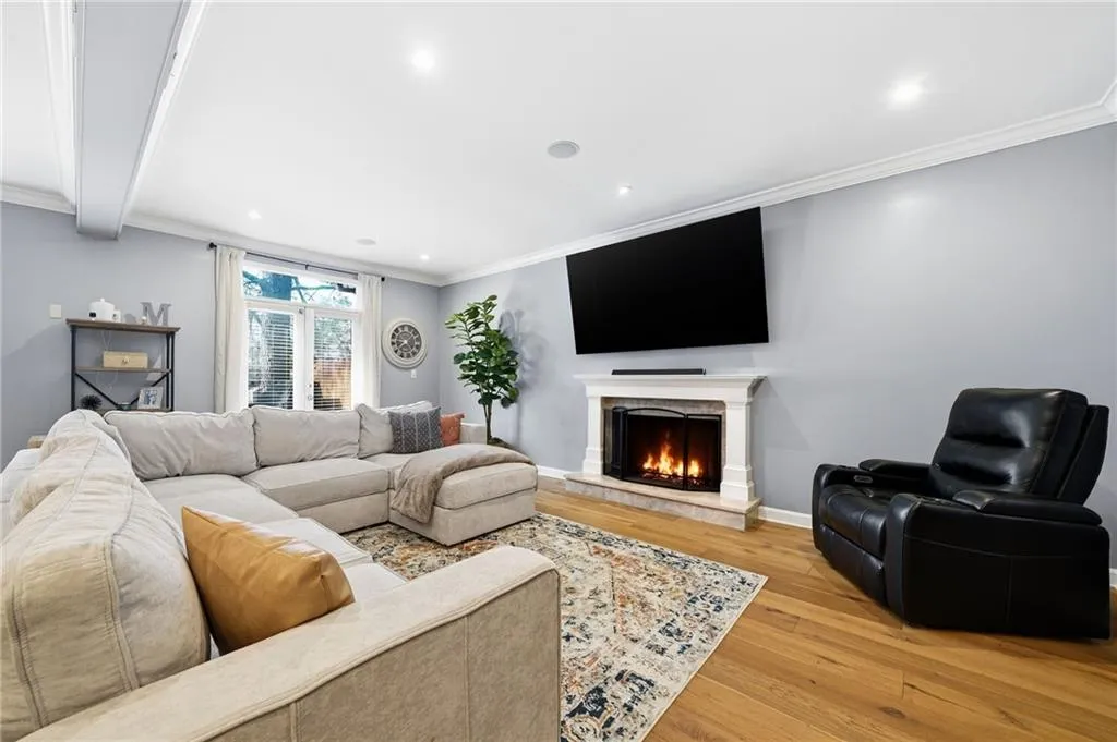 Living area with ornamental molding, light wood-style floors, a warm lit fireplace, and recessed lighting