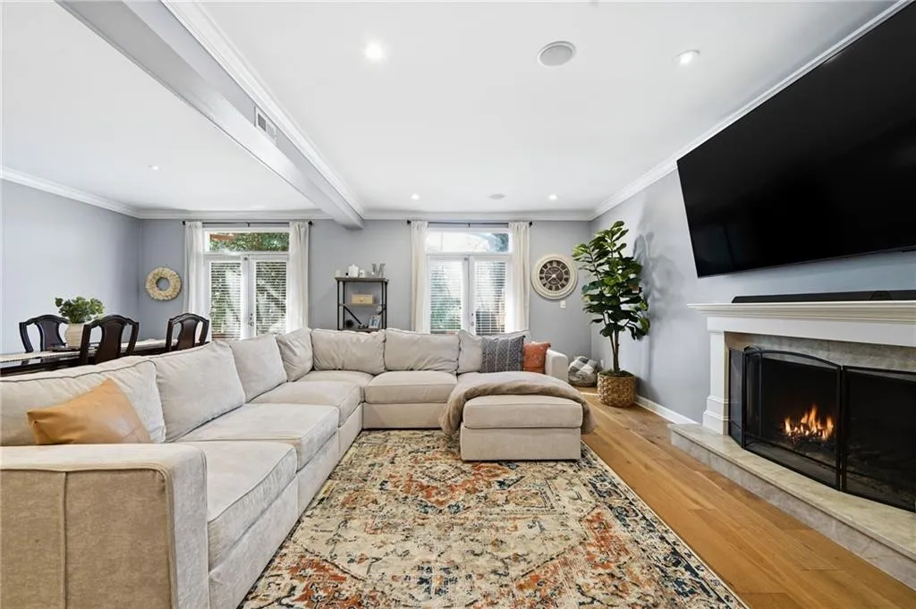 Living area with light wood-style flooring, beam ceiling, a warm lit fireplace, crown molding, and plenty of natural light