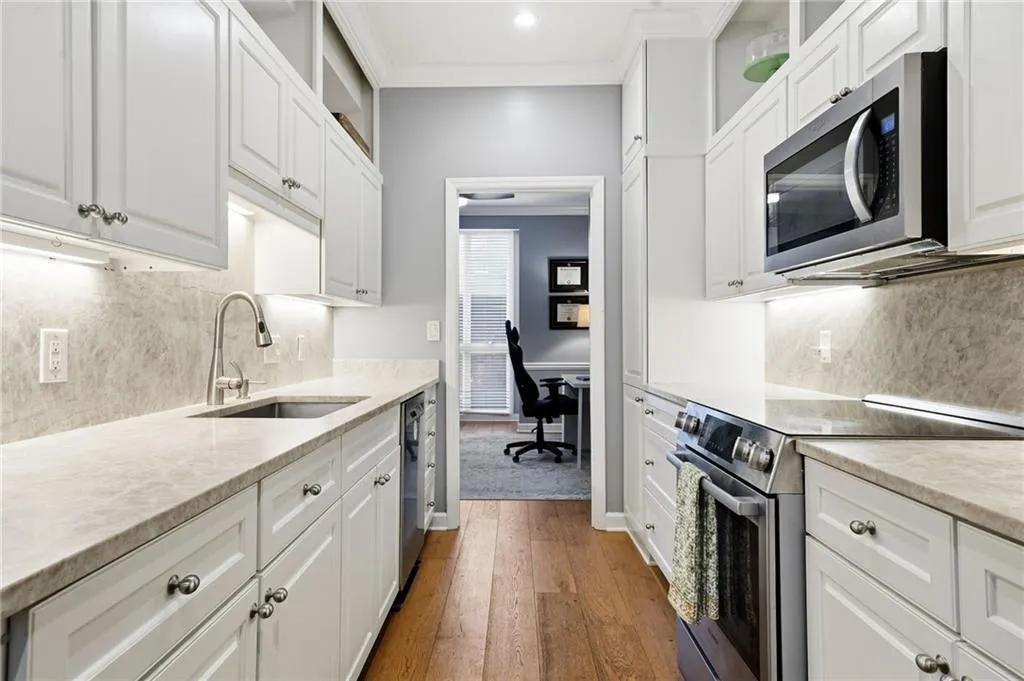 Kitchen with crown molding, stainless steel appliances, white cabinets, backsplash, and an office area