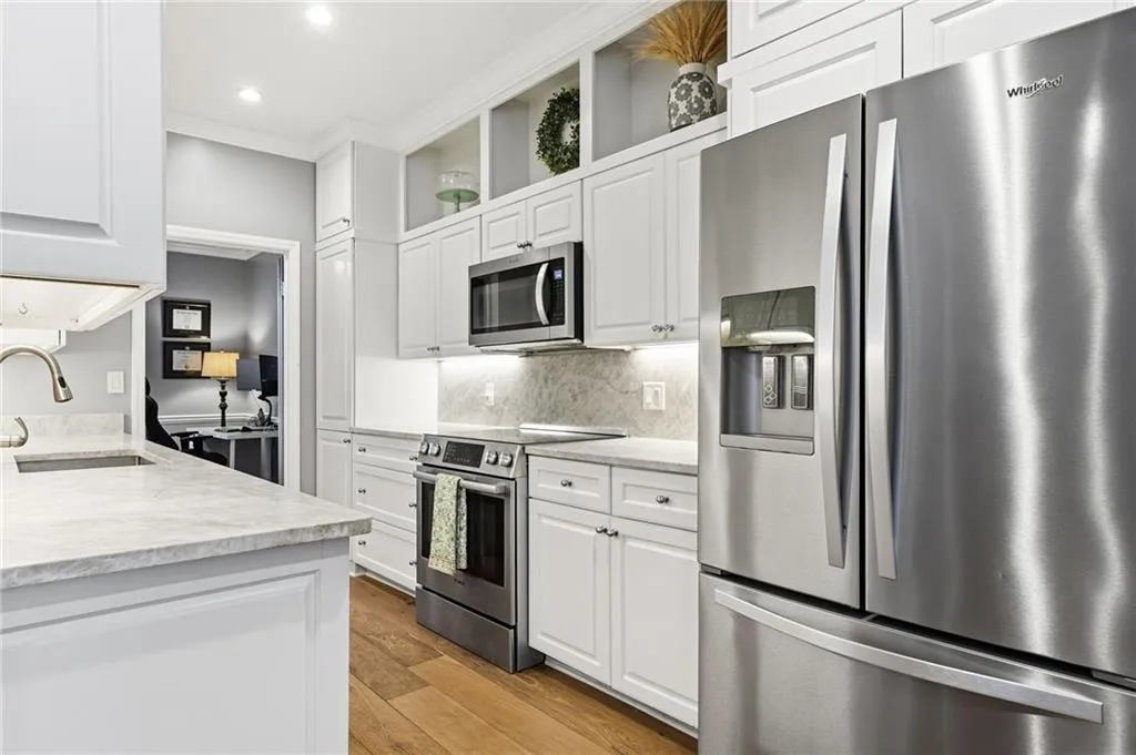 Kitchen with open shelves, stainless steel appliances, light wood finished floors, white cabinetry, and light stone counters