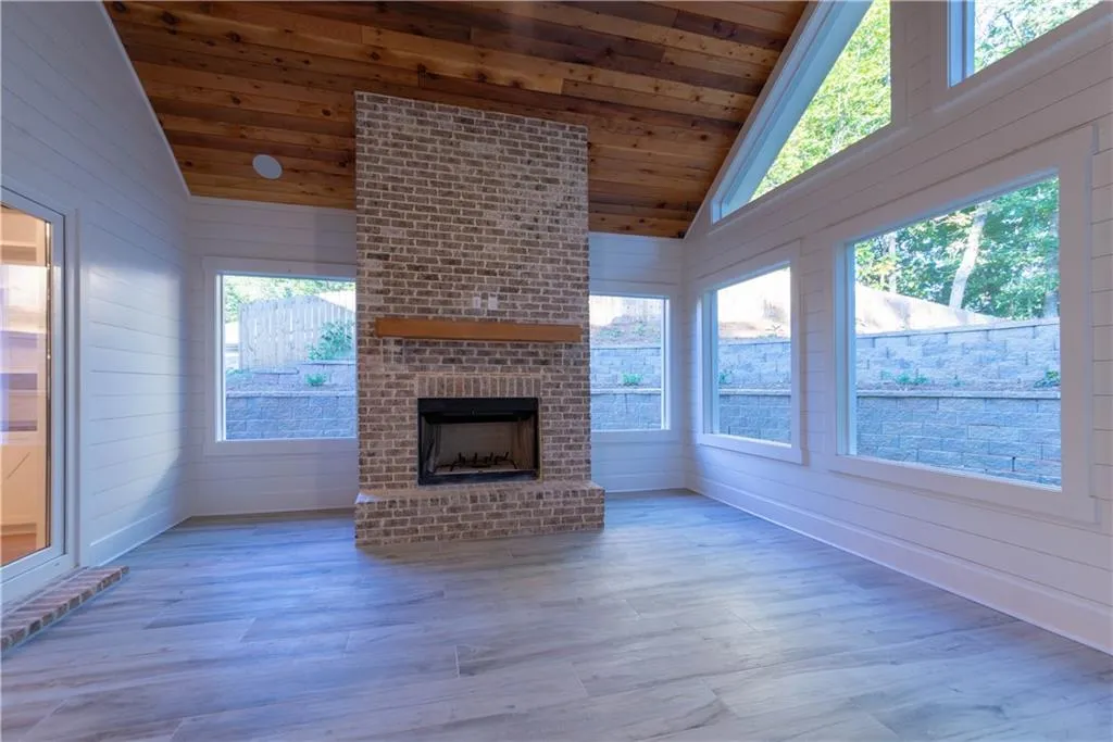 Unfurnished living room featuring an outdoor brick fireplace, wooden ceiling, light hardwood / wood-style flooring, and vaulted ceiling