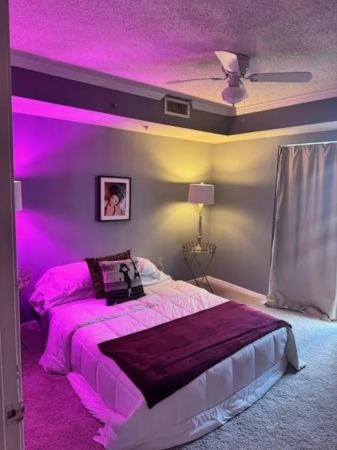 Carpeted bedroom with ceiling fan, ornamental molding, and a textured ceiling