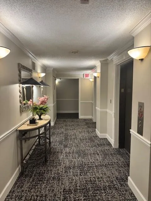 Hallway featuring dark carpet, a textured ceiling, and ornamental molding