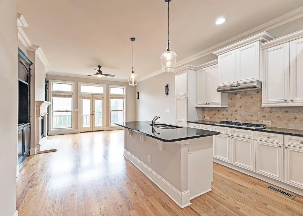 Open Plan Living/Family Room And Kitchen Area Featuring Built In Bookcases, Fireplace, Crown Molding, Ceiling Fan, and Light Hardwood Floors.