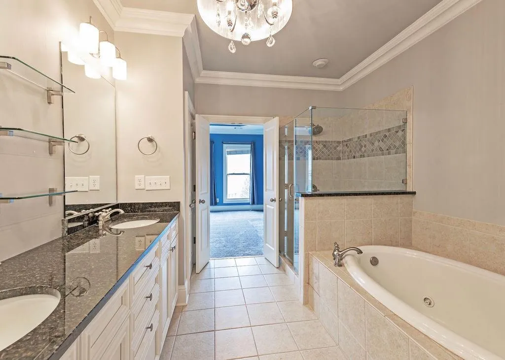 Bathroom Featuring Double Vanity, Crown Molding, Tiled Floors, Separate Shower and Jetted Soaking Tub, and Chandelier.