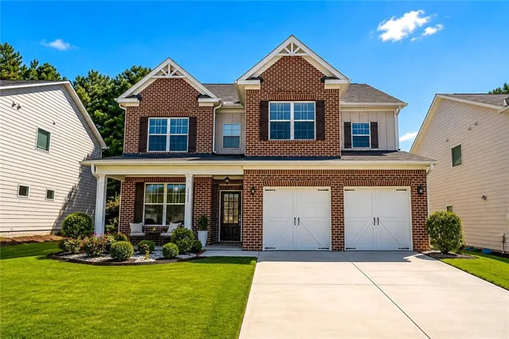 Brick and siding exterior with a covered front porch, two-car garage with carriage-style doors, concrete driveway, and established landscaping