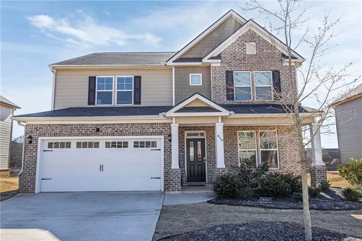 Two-story property featuring brick and siding exterior, a two-car garage with decorative hardware, an inviting covered entry with columns, and established front landscaping